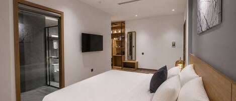 A modern hotel room with a large bed, a television, a wardrobe, and a glass shower enclosure.