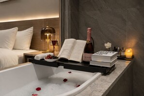 Une salle de bain moderne avec une baignoire, un livre, une bouteille de vin et une bougie posés sur le comptoir.
