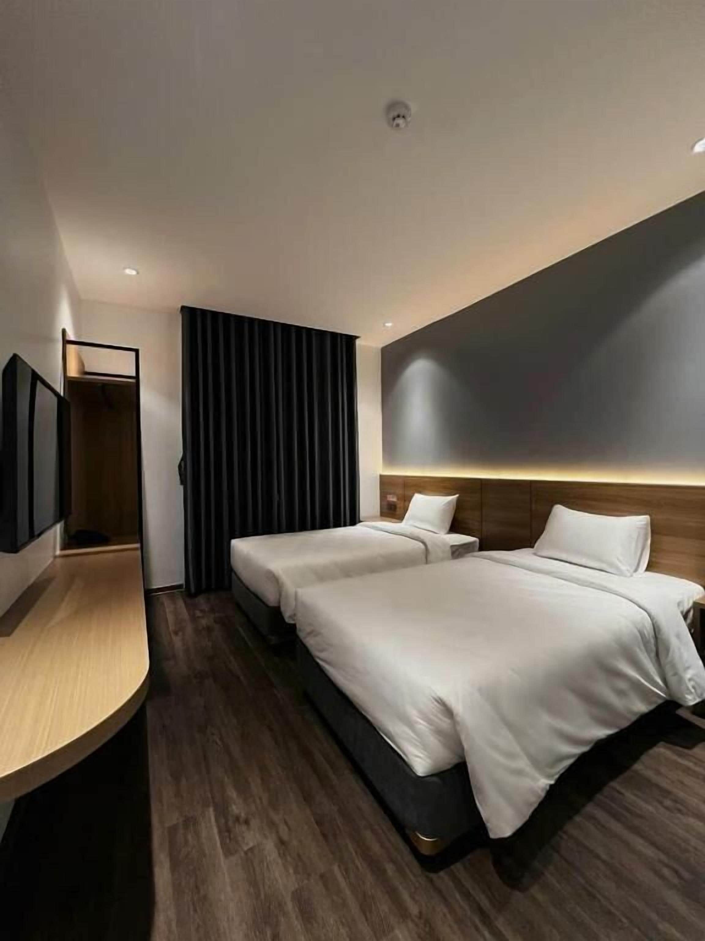 Een hotelkamer met twee bedden, een houten bureau, een flatscreen televisie en een donkerkleurig gordijn.