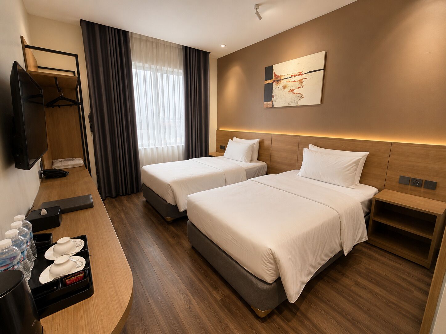 Ein Hotelzimmer mit zwei Betten, einem Fernseher, einem Schreibtisch mit Kaffeemaschine und einem Bild an der Wand.