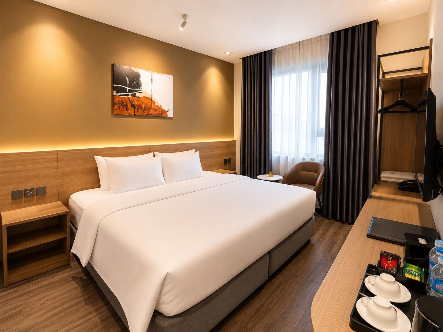 Quarto de hotel com cama grande, mesas de cabeceira, escrivaninha com cadeira, televisão e um quadro na parede.
