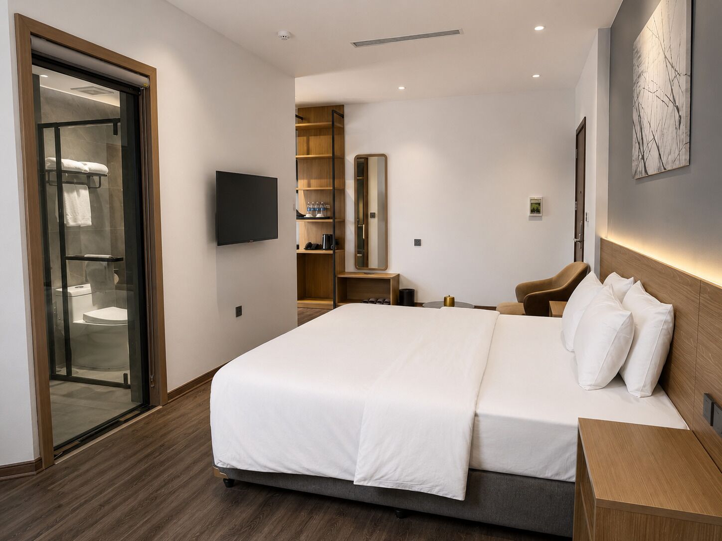 Une chambre d’hôtel moderne dotée d’un grand lit, d’une télévision, d’un coin salon et d’une salle de bain avec une porte en verre.