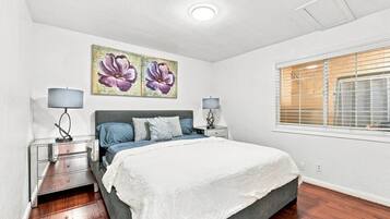 Une chambre à coucher comprenant un lit, deux tables de chevet, une fenêtre avec des stores et un luminaire au plafond.