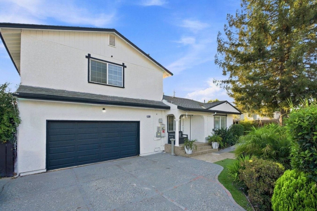 A two-story residential building with a garage, a front porch, and a well-maintained garden.