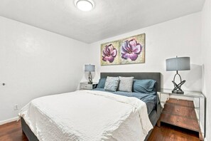 A bedroom with a bed, two bedside tables, a nightstand, and a wall-mounted lamp.