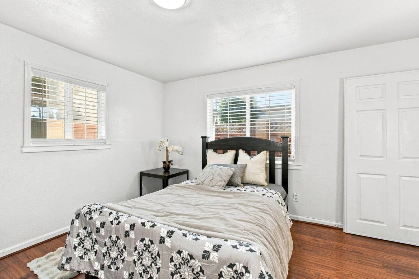 A bedroom with a bed, two windows, a nightstand, and a door.