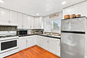 Una cocina con armarios blancos, un refrigerador de acero inoxidable, un microondas y una estufa.