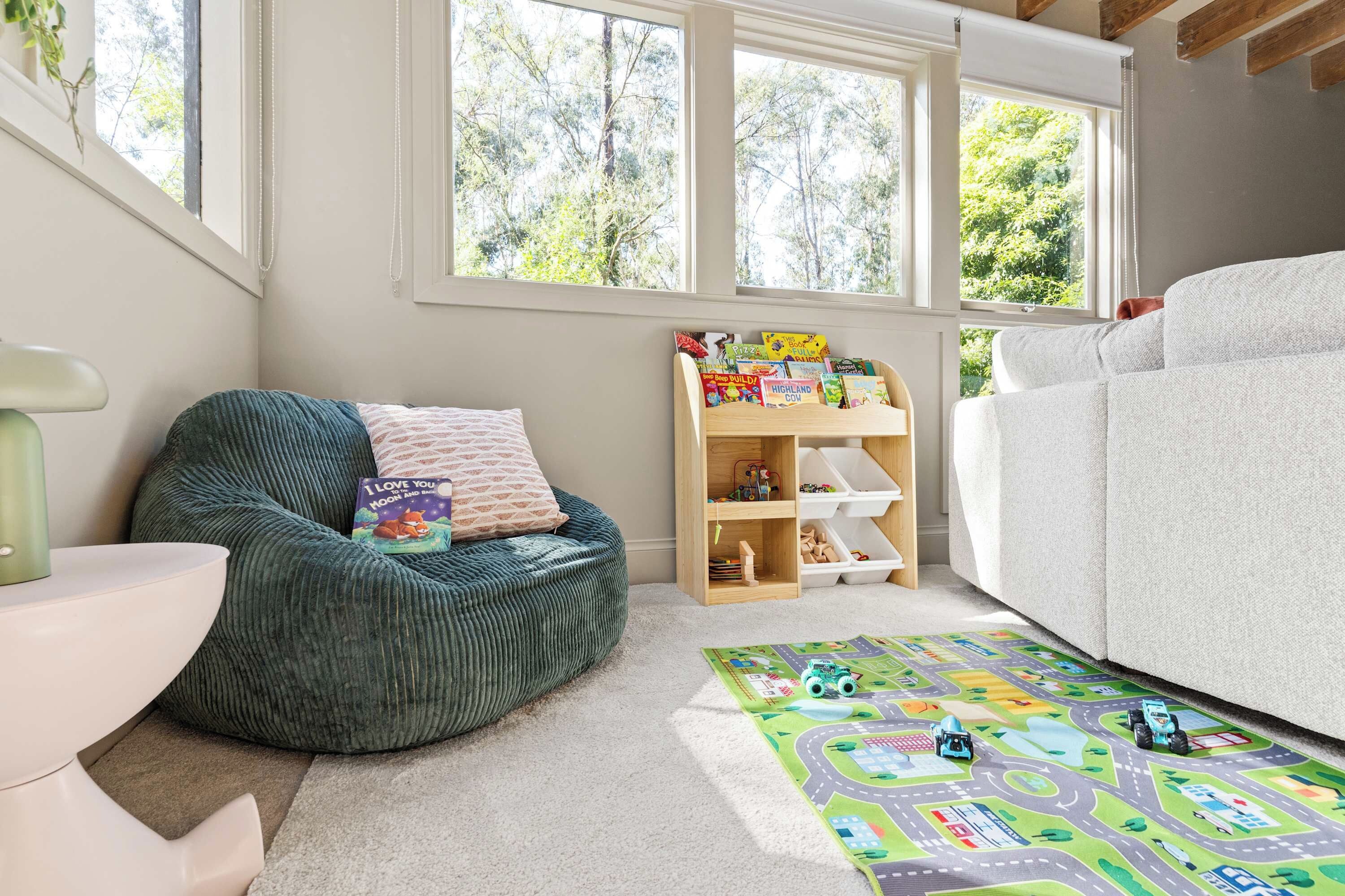 A child's playroom with a green bean bag chair, a bookshelf with children's books, a white sofa, and a play mat.