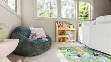 A child's playroom with a green bean bag chair, a bookshelf with children's books, a white sofa, and a play mat.
