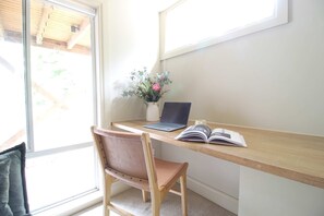 A workspace with a wooden desk, a laptop, an open book, and a vase with flowers.
