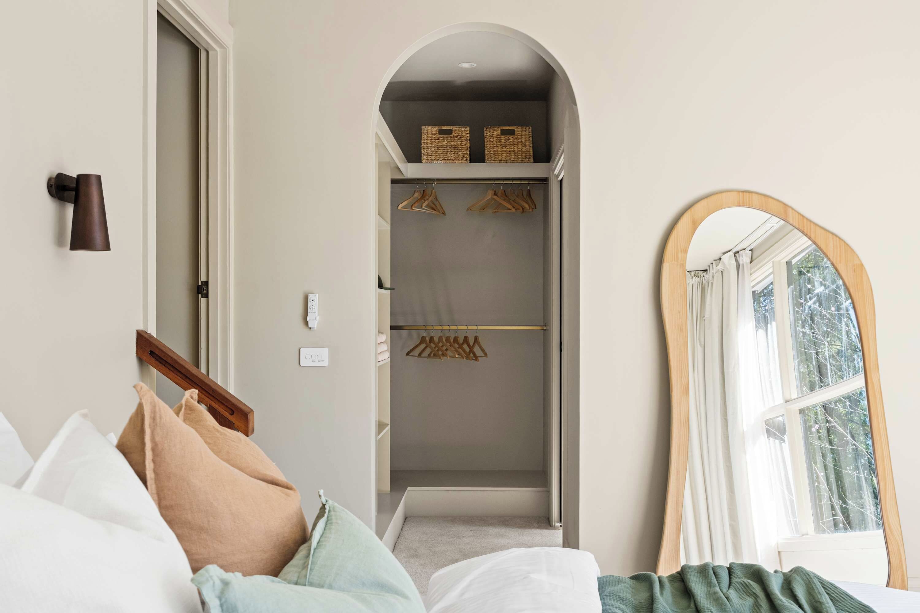 A hotel room with a bed, a wooden coat rack, a mirror, and a walk-in closet with hanging clothes.
