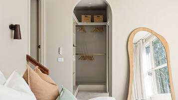A hotel room with a bed, a wooden coat rack, a mirror, and a walk-in closet with hanging clothes.