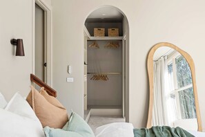Ein Hotelzimmer mit einem Bett, einem Holz-Kleiderständer, einem Spiegel und einem begehbaren Kleiderschrank mit Kleidung.
