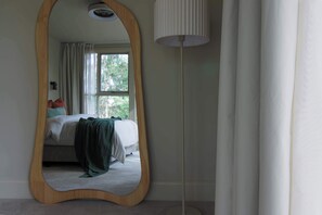 A bedroom with a bed, a mirror, and a floor lamp.