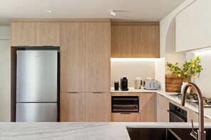A modern kitchen with wooden cabinets, a stainless steel refrigerator, a coffee maker, a toaster, and a gas stove.