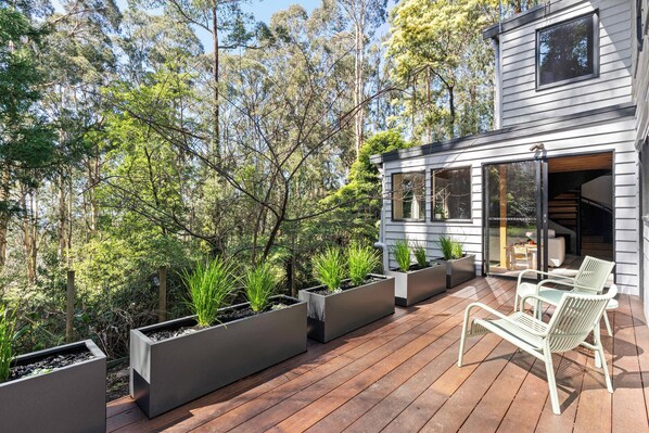 A modern house with a deck, outdoor seating, and a garden with planters.