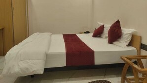 Una cama individual con colcha blanca y roja, dos almohadas y una silla de madera.