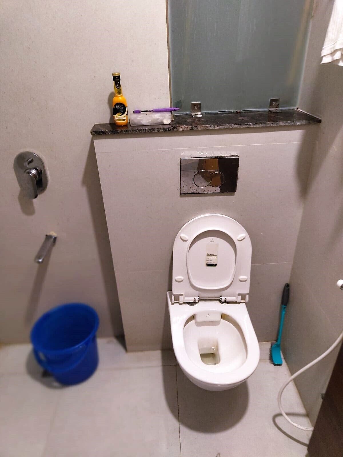 A small bathroom with a toilet, a blue bucket, and a toothbrush.
