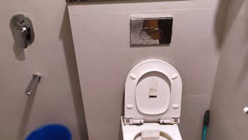 A small bathroom with a toilet, a blue bucket, and a toothbrush.