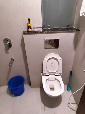 Un baño pequeño con un inodoro, un cubo azul y un cepillo de dientes.