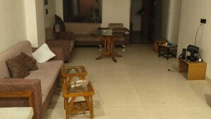 Sala de estar con sofá, mesa de centro y sillas. Hay un televisor y un detector de incendios rojo en la pared.