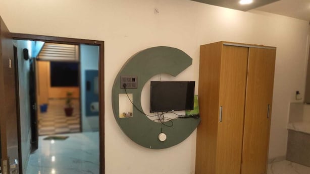 Una habitación con un amplio adorno en forma de G en la pared, un televisor fijado a la pared y un armario de madera.