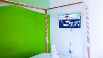 Quarto com parede verde, cama com roupa de cama branca, televisão montada e uma tomada.
