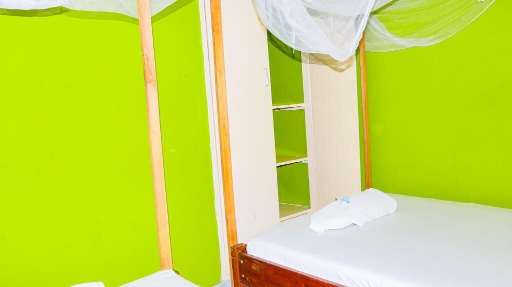 A room with a bed, a white curtain, and a green wall.
