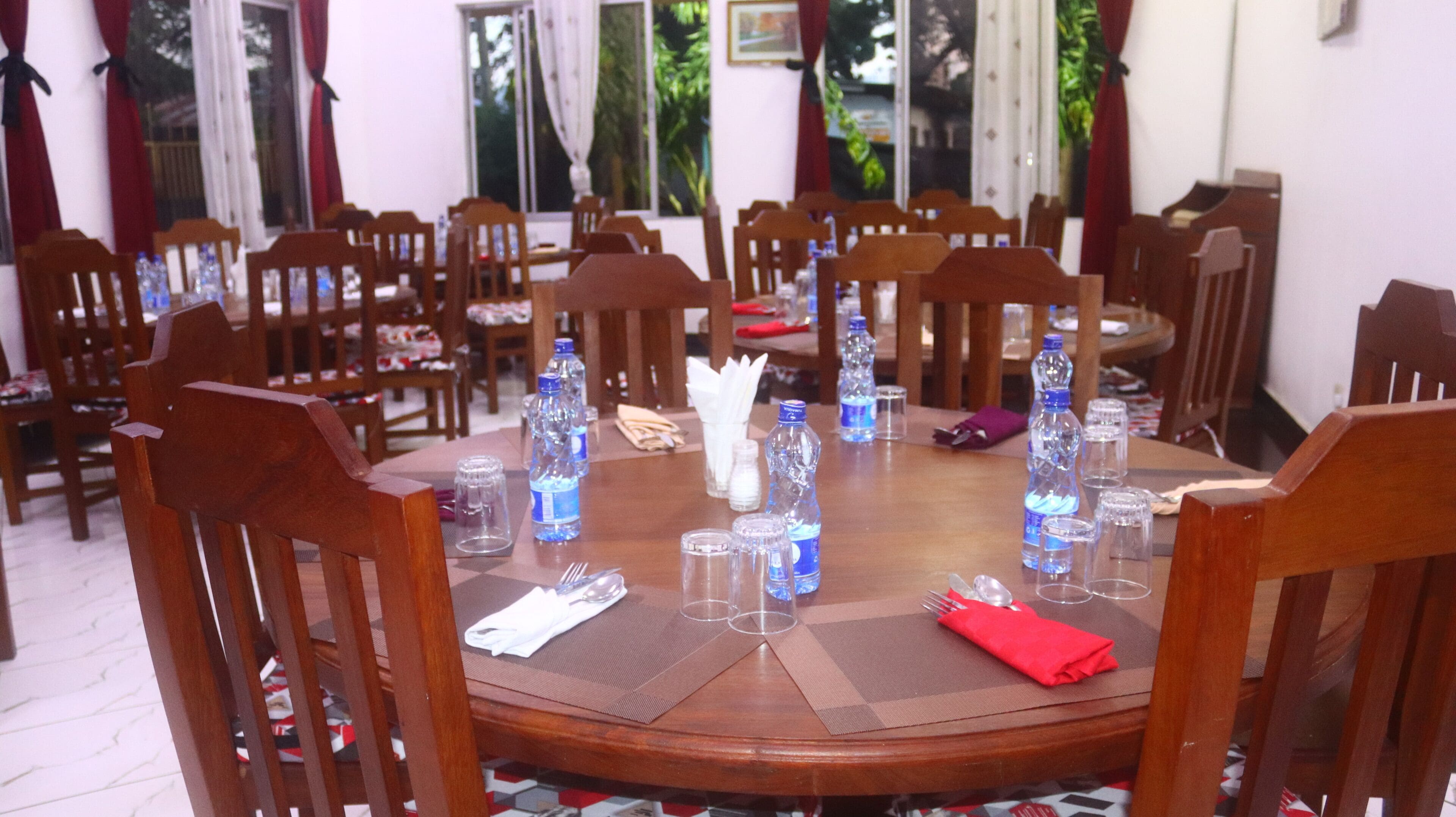 Una mesa de madera redonda con sillas a su alrededor, dispuesta con botellas de agua, vasos y servilletas.