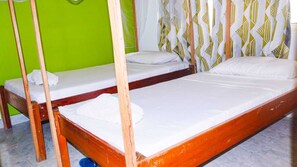 Una habitación con dos camas de madera, una pared verde y cortinas estampadas.