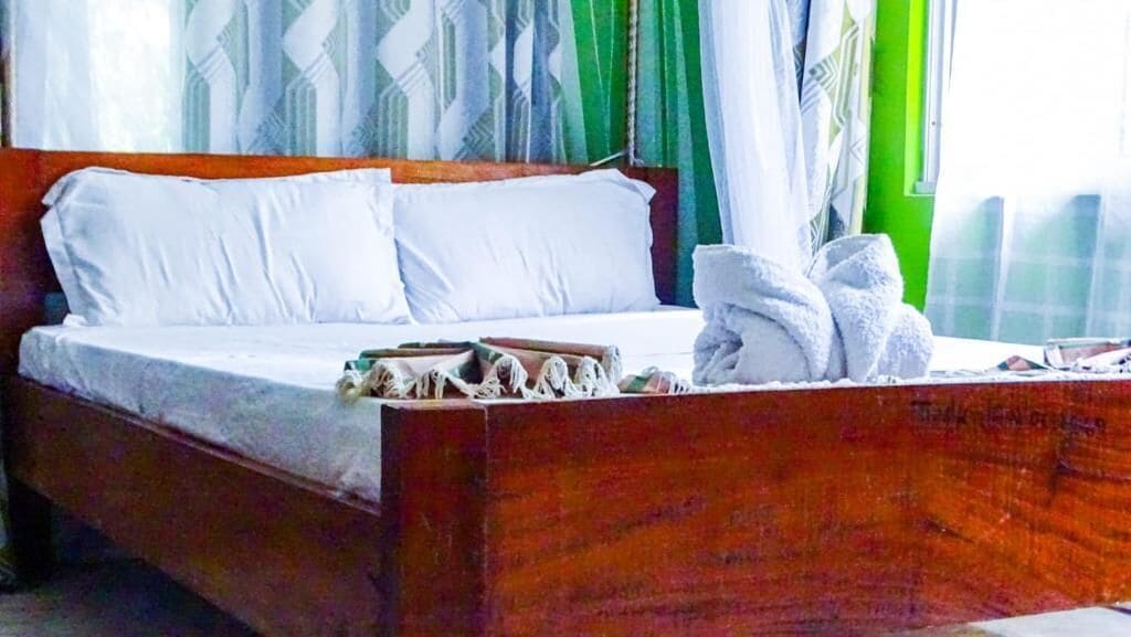 Una cama con sábanas blancas, cabecera de madera y una pila de toallas dobladas.