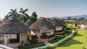 A row of thatched-roof cottages with a paved pathway leading through a well-maintained garden. - forest mud villas (Haridwar)
