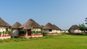 A row of thatched-roof cottages with a well-maintained lawn and potted plants. - forest mud villas (Haridwar)