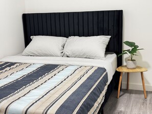 A bed with a black headboard, striped bedding, and a small wooden side table with a plant.