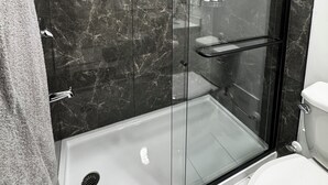 A modern bathroom with a glass-enclosed shower, a toilet, and marble walls.