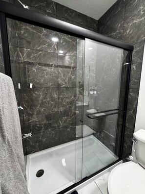 Een moderne badkamer met een douchecabine, toilet en marmeren wanden.