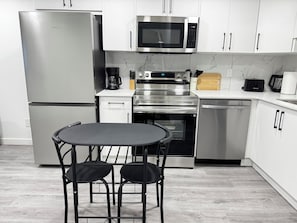 A modern kitchen with stainless steel appliances, a marble backsplash, and a dining area with a table and chairs.