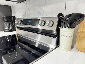 A stainless steel range with a digital display, a coffee maker, and a utensil holder on a kitchen counter.