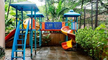 Un parque infantil con toboganes y estructuras para escalar, rodeado de follaje.
