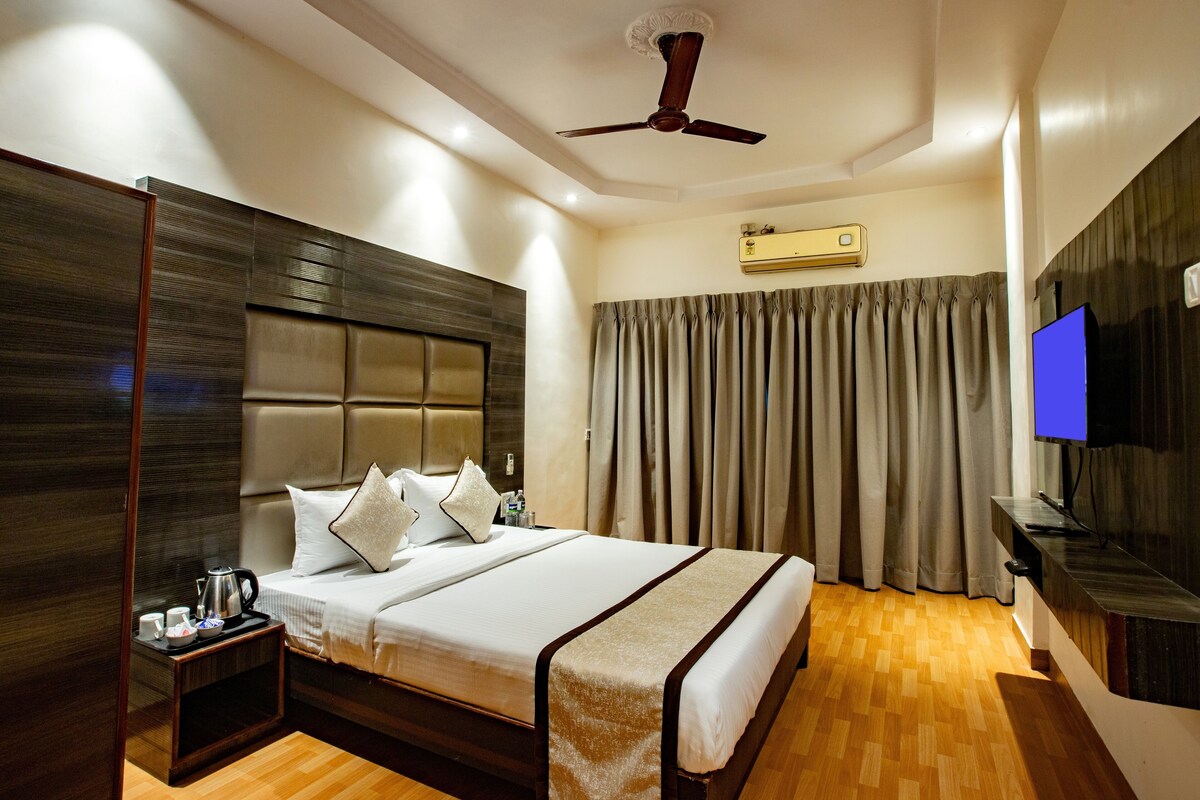Une chambre d’hôtel avec un grand lit, une table de chevet équipée de divers accessoires, un ventilateur de plafond, un appareil de climatisation, une télévision et un rideau.