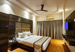 Une chambre d’hôtel avec un grand lit, une table de chevet équipée de divers accessoires, un ventilateur de plafond, un appareil de climatisation, une télévision et un rideau.