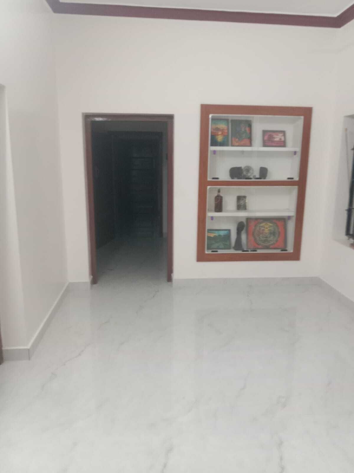 Un pasillo con piso de mármol que conduce a una puerta, un estante en la pared con varios objetos y una pared blanca lisa.