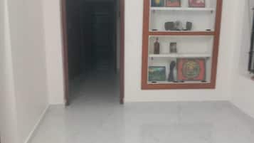 Un pasillo con piso de mármol que conduce a una puerta, un estante en la pared con varios objetos y una pared blanca lisa.