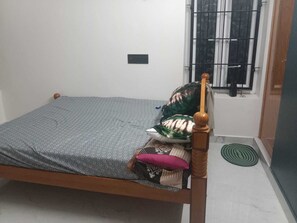 A single bed with a wooden frame, a grey patterned mattress, and a wooden headboard. - Mangai Homestay — A Quiet, Nature-Led Stay in Tiruchendur (Thiruchendur)