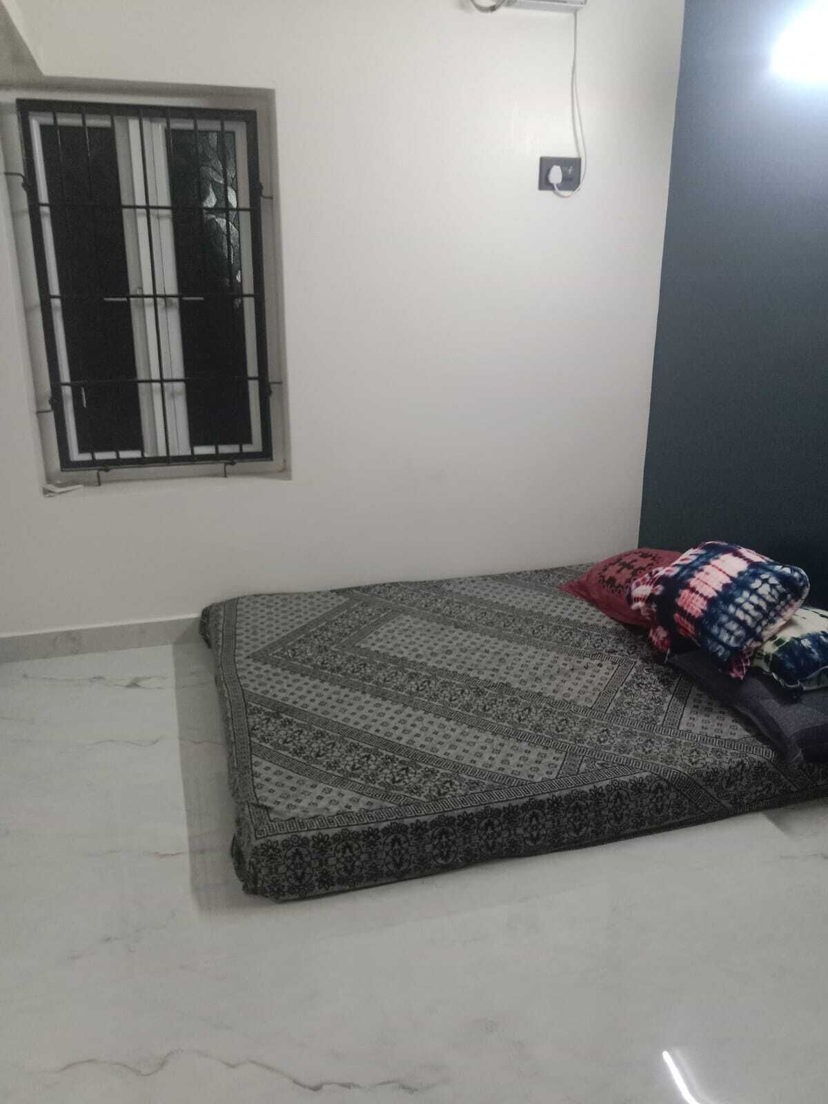 Una stanza con un letto, una finestra con inferriate, una lampada a parete e un pavimento piastrellato.