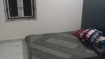 Una stanza con un letto, una finestra con inferriate, una lampada a parete e un pavimento piastrellato.