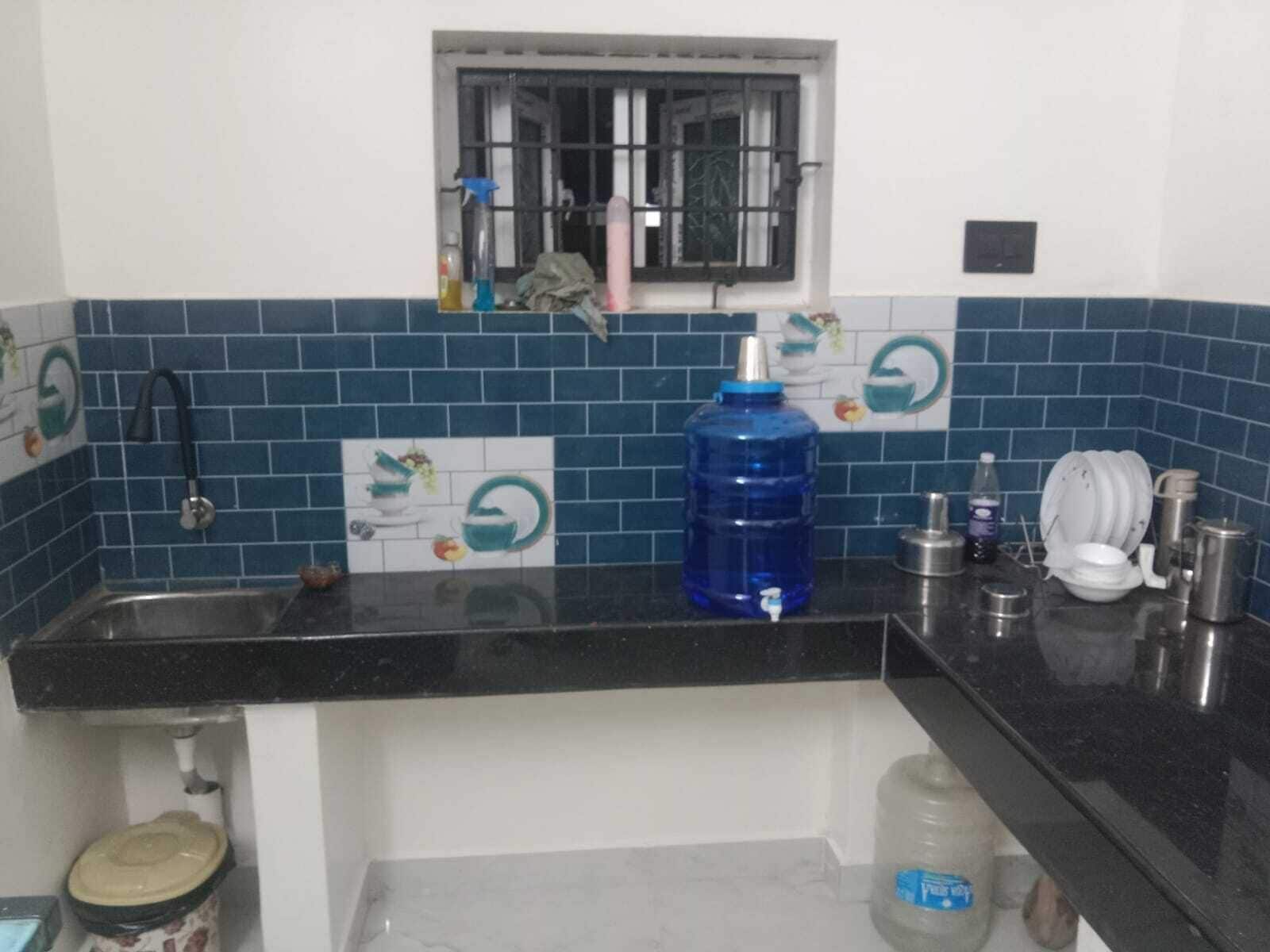 Eine Küche mit einer schwarzen Arbeitsplatte, einem blauen Wasserspender, einem Spülbecken und einem Fenster mit Gitterstäben.