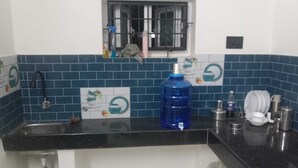 Cozinha com bancada preta, dispenser de água azul, pia e janela com grades.