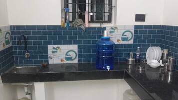 Eine Küche mit einer schwarzen Arbeitsplatte, einem blauen Wasserspender, einem Spülbecken und einem Fenster mit Gitterstäben.