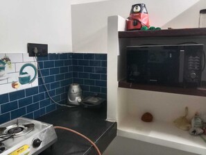 A kitchen with a gas stove, a microwave, and a kettle on the countertop. - Mangai Homestay — A Quiet, Nature-Led Stay in Tiruchendur (Thiruchendur)